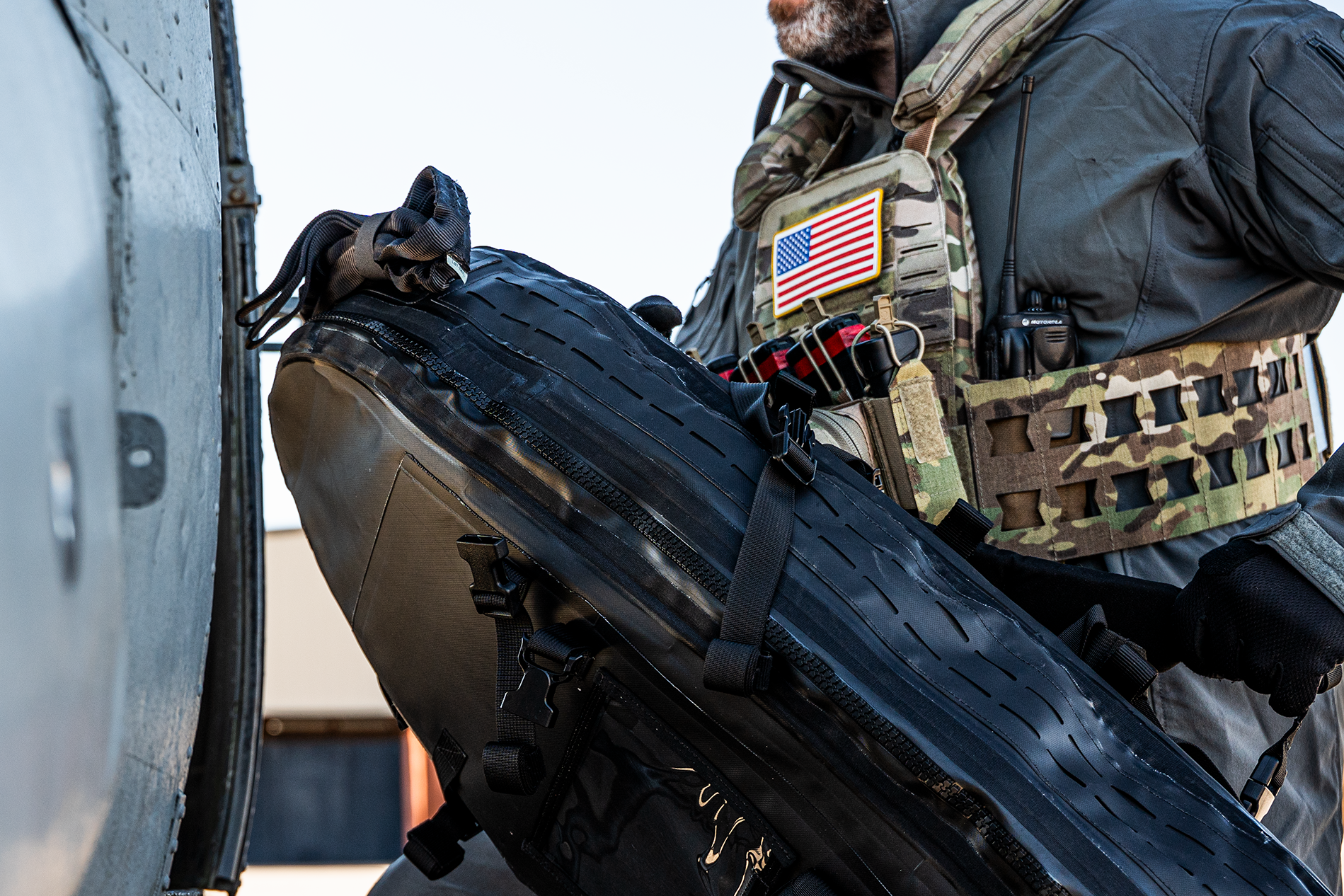 Person in tactical gear holding a large black object, with an American flag patch visible.